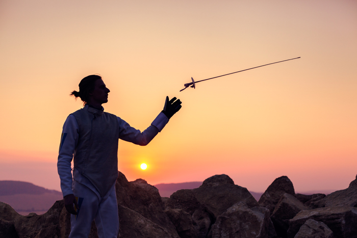 A fencer throwing his sword in the air with a sunset background