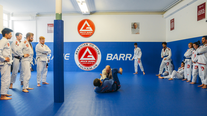 This is a Brazilian jiu-jitsu academy with students gathering to watch a technique demonstration
