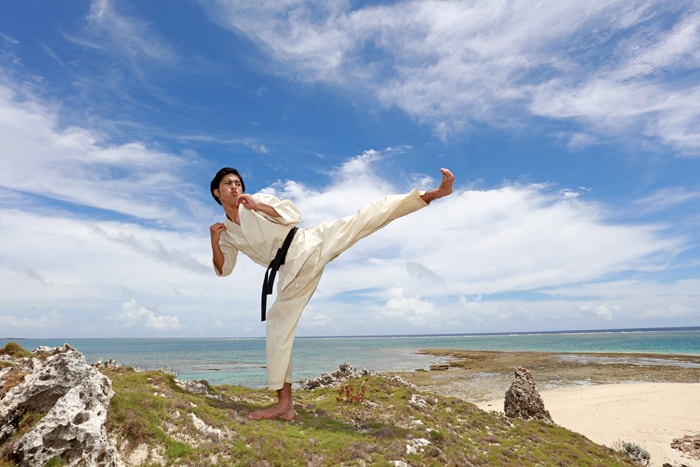 A karateka performing a kick on a beach