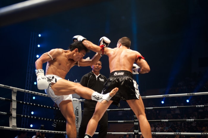 This is a kickboxing fight taking place inside a ring, with one fighter throwing a punch while the other attempts a low kick