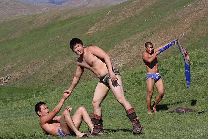 Photo of two Mongolian wrestlers, one is helping the other get up from the ground